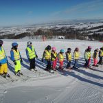 Grupa zaawansowana słucha instrukcji przed wykonaniem kolejnego ćwiczenia doskonalącego technikę jazdy na nartach.