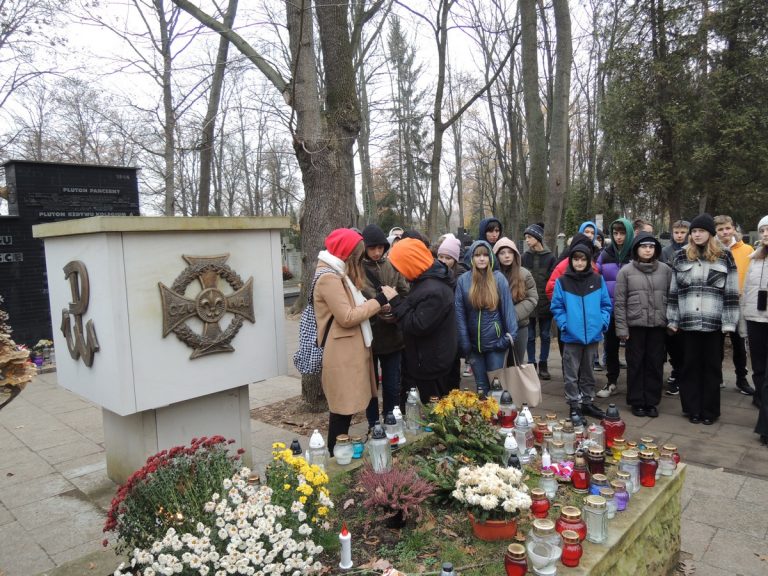 Grupa przy grobie Aleksandra Kamińskiego zapala znicz.
