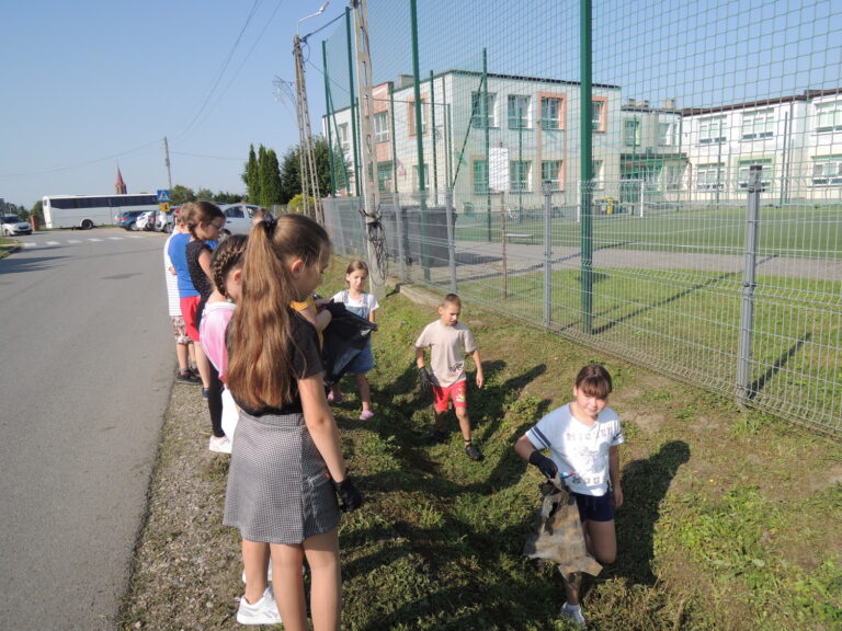 Klasa trzecia porządkuje teren wzdłuż szkolnego ogrodzenia.
