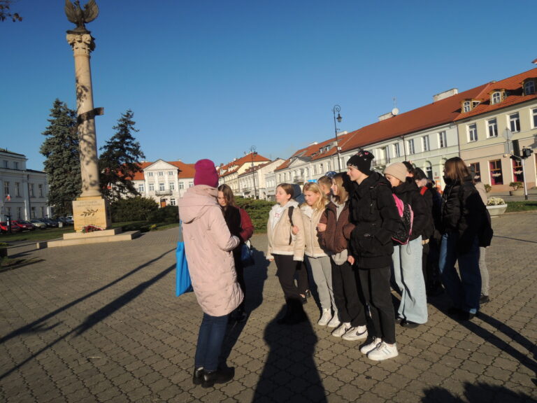 Uczniowie z przewodnikiem na placu Gabriela Narutowicza słuchają opowieści o historii Płocka.
