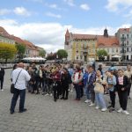 Uczestnicy wycieczki słuchają opowieści przewodnika na starym rynku w Gnieźnie.
