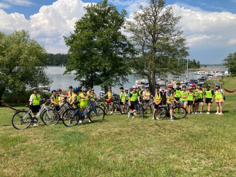 Pamiątkowa fotografia uczestników wycieczki rowerowej na tle portu w miejscowości Wierzba.