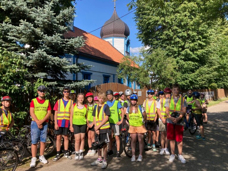 Pamiątkowa fotografia uczestników wycieczki rowerowej przy cerkwi  prawosławnej w Wojnowie.