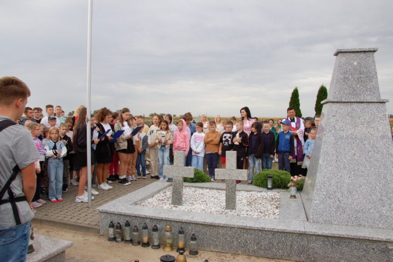 Uczniowie szkoły wraz z nauczycielami zgromadzeni przy kwaterze poległych.