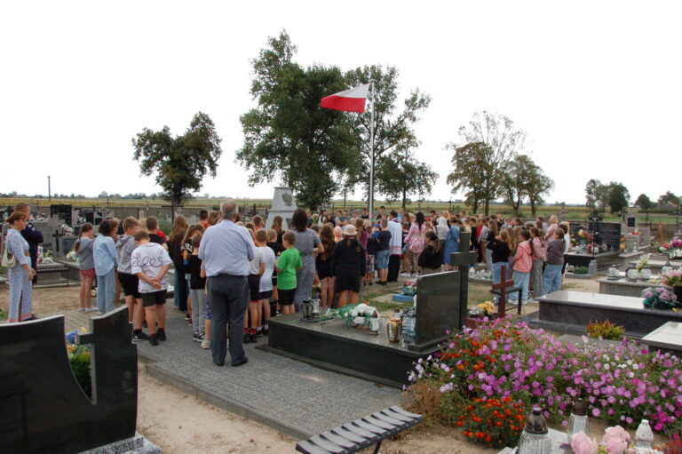 Uczniowie szkoły wraz z nauczycielami zgromadzeni przy kwaterze poległych.