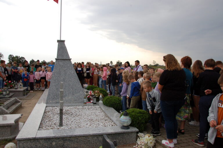 Uczniowie szkoły wraz z nauczycielami zgromadzeni przy kwaterze poległych.