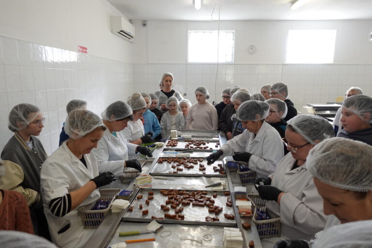 Uczestnicy wycieczki obserwują pracę pań ręcznie zawijających cukierki.
